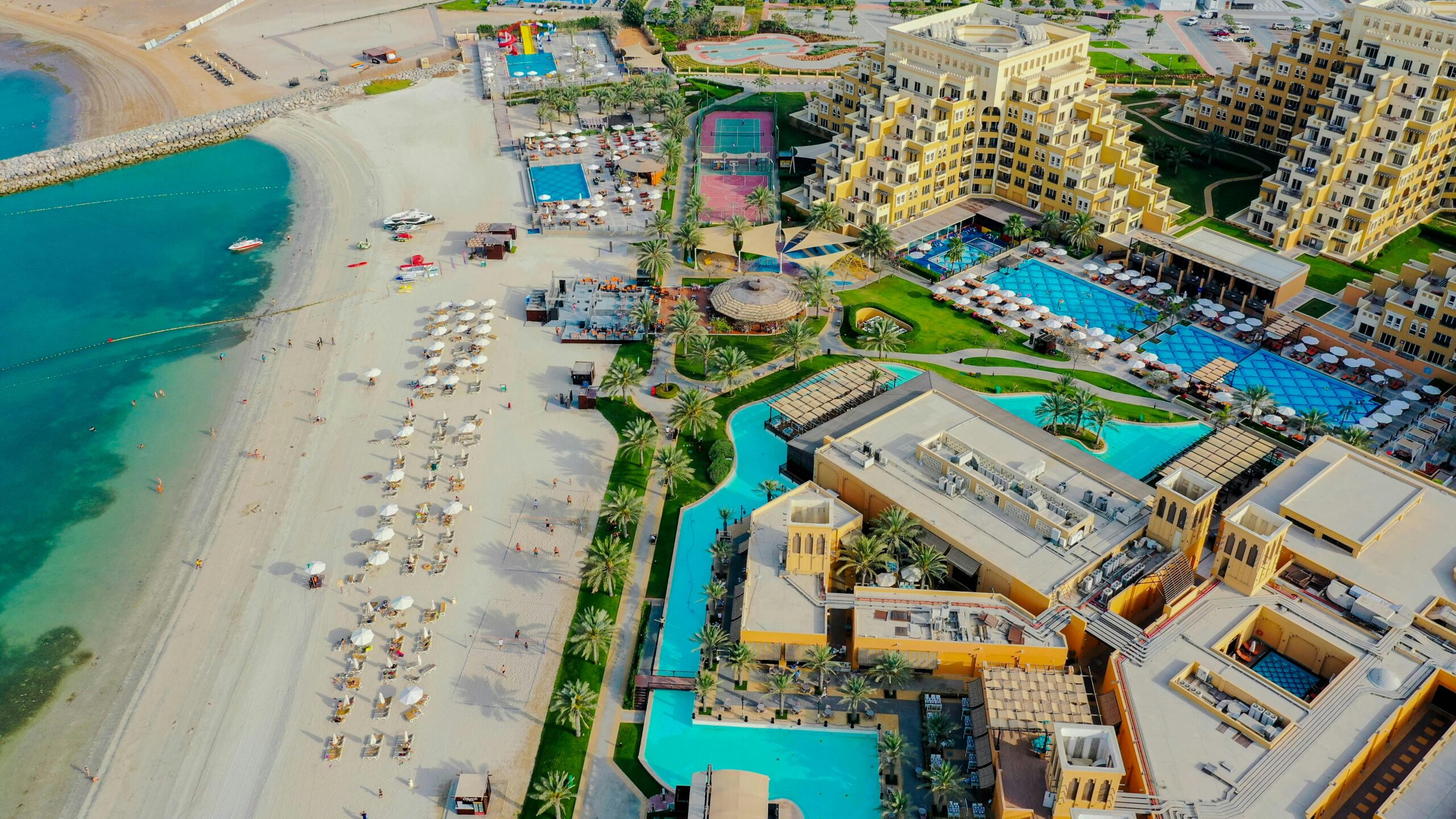 Aerial view of a luxurious beach resort in Ras al Khaimah, UAE, showcasing pools, palm trees, and pristine coastline.
